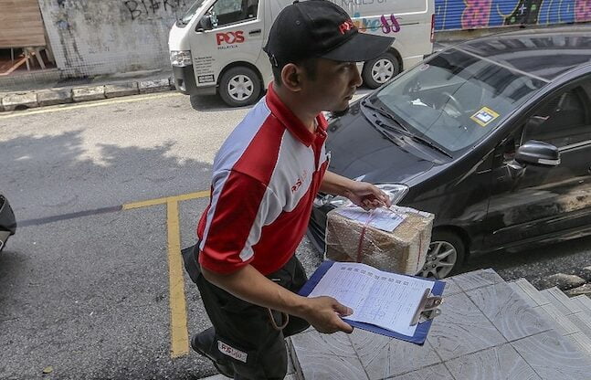 Seorang pekerja Pos Malaysia sedang bertugas. - Foto ihsan Malay Mail